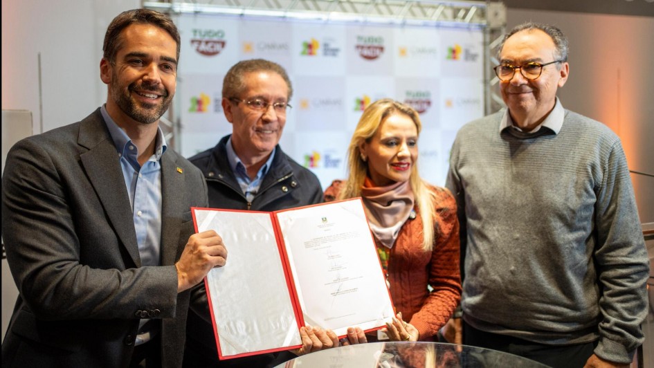 Foto posada de Leite, Danielle e mais dois homens exibindo o documento assinado e sorrindo para a câmera, num ambiente fechado