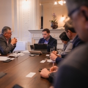 Foto em sala de reunião, com seis pessoas ao redor de uma mesa retangular de madeira. Gabriel aparece ao centro da imagem, conversando com os presentes.