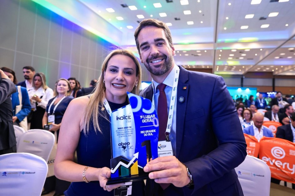 Foto do governador Eduardo Leite e da titular da SPGG, Danielle Calazans, segurando o troféu. Ambos sorriem para a câmera. No troféu, pode-se ler a inscrição "1º lugar geral - Rio Grande do Sul". Ao fundo, sem foco, há diversas pessoas.