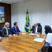 Foto de uma sala de reunião formal, com cinco pessoas sentadas ao redor de uma mesa de maneira. Leite aparece ao centro, olhando para Alkmin, que fala. 