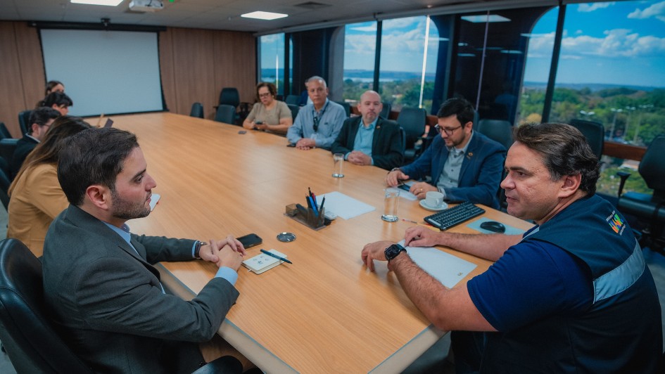 A foto mostra um grupo de várias pessoas sentadas ao redor de uma mesa de conferência em uma sala de reuniões. O vice-governador Gabriel Souza está no lado esquerdo da mesa, e o secretário nacional de Transporte Ferroviário, Leonardo Ribeiro, está no lado oposto, de frente para a câmera. Todos estão prestando atenção à discussão.