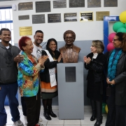 Diversas pessoas estão reunidas em torno do busto recém-inaugurado do poeta Oliveira Silveira. Elas batem palmas e sorriem para a foto. 