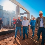 Um grupo de pessoas, com o vice-governador ao centro, caminha em meio a um canteiro de obras na escola.