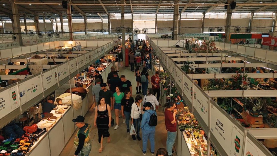 Foto geral do pavilhão. No centro do quadro, está um corredor enquadrado levemente por cima, com várias pessoas caminhando. Ao redor, os estandes, de cor branca, com produtos em exibição nas bancadas.