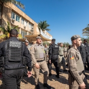 Foto mostra fileiras de policiais que se cruzam em alinhamento. À esquerda da foto, está o prédio da Cadeia Pública de Porto Alegre, com fachada em amarelo e bege. Marcham em direção ao prédio, de costa para a foto, os policiais penais, com uniformes pretos. Em alguns é possível ver nas costas o emblema da Polícia Penal. No outro sentido, em direção ao jardim, marcham os policiais militares, com uniformes beges e boinas também beges.