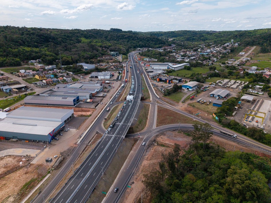 Vista aérea de um grande cruzamento de rodovias, com pontes e viadutos sobrepostos. Há carros circulando nas pistas e uma tenda branca montada sobre uma das pontes. Ao redor, há prédios comerciais, estacionamentos e algumas casas ao fundo.