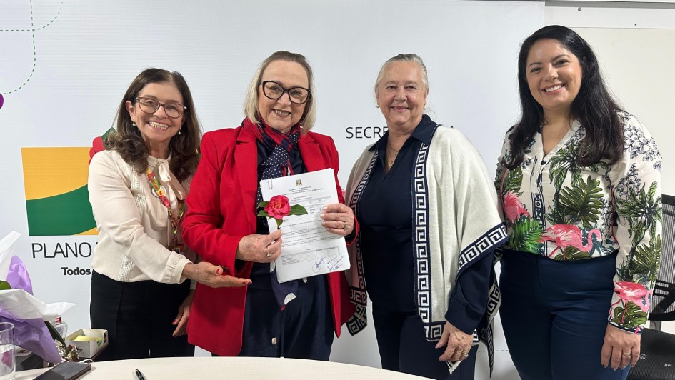 Foto mostra a secret&aacute;ria Arita Bergmann com representantes do Hospital Santo Ant&ocirc;nio, de Tenente Portela. Arita est&aacute; de casaco vermelho, e segura um documento na m&atilde;o esquerda e uma rosa na outra m&atilde;o. Duas mulheres est&atilde;o &agrave; sua esquerda. Ao lado direito da secret&aacute;ria, est&aacute; uma servidora do estado. As quatro sorriem para a c&acirc;mera.