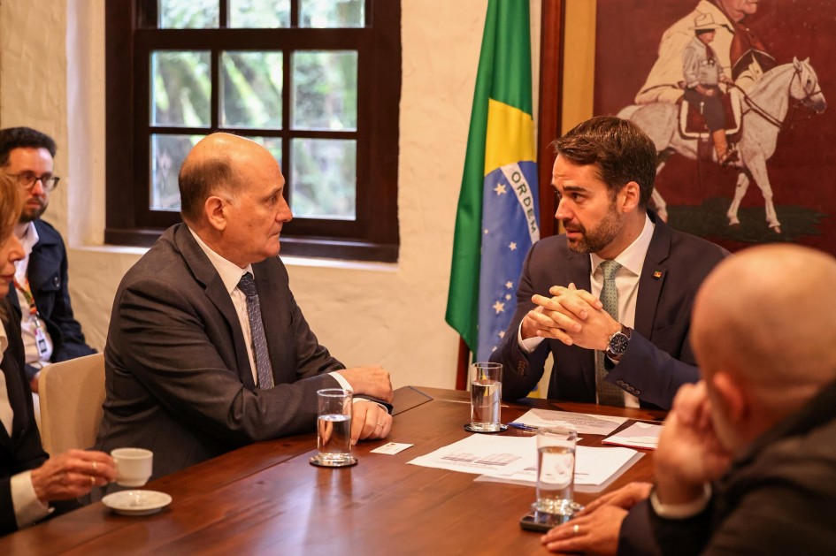 Foto mostra o governador Eduardo Leite conversando com o embaixador, sentados à mesa. Ao fundo, a bandeira do Brasil e um quadro de um ginete sobre cavalo.