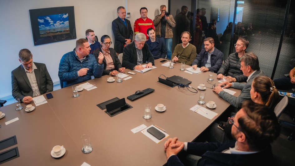 A imagem mostra uma sala de reuniões com uma grande mesa de conferência onde várias pessoas estão sentadas, incluindo o vice-governador Gabriel Souza. Ao redor da mesa, outras pessoas em trajes formais também participam da reunião, com papéis e copos à sua frente.