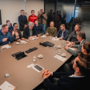 A imagem mostra uma sala de reuniões com uma grande mesa de conferência onde várias pessoas estão sentadas, incluindo o vice-governador Gabriel Souza. Ao redor da mesa, outras pessoas em trajes formais também participam da reunião, com papéis e copos à sua frente.