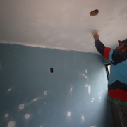 Foto interna de um trabalhador em uma escala, lixando o teto de cor branca da unidade. As paredes são azuis.