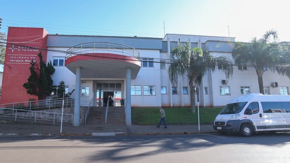 Foto da fachada do Hospital São Vicente de Paulo. Ao lado esquerdo, em uma torre vermelha, é possível ler o nome da instituição. O hospital está pintado em tons de cinza e branco. Há duas árvores na frente da instituição. 