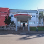 Foto da fachada do Hospital São Vicente de Paulo. Ao lado esquerdo, em uma torre vermelha, é possível ler o nome da instituição. O hospital está pintado em tons de cinza e branco. Há duas árvores na frente da instituição. 