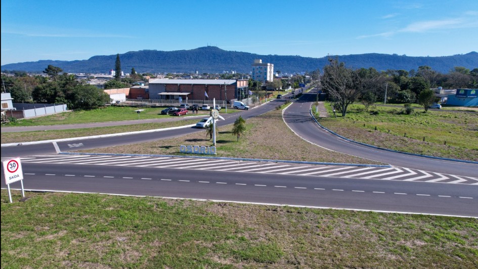 Foto aérea em menor altitude mostra parte da nova via asfaltada, com sinalização horizontal branca e placas de trânsito. Em primeiro plano, uma placa indica limite de velocidade de 30 km/h. Ao fundo, é possível ver o letreiro “Osório” no canteiro central e a cidade ao pé de uma serra.