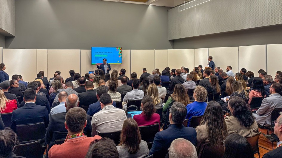 Imagem mostra palestra na oficina em frente a telão, plateia de costas acompanha a apresentação.