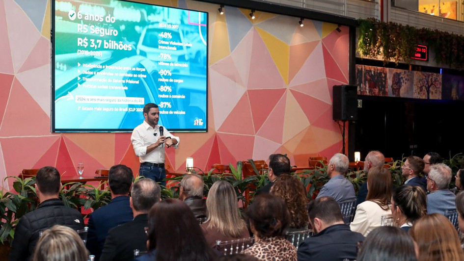 A imagem apresenta um evento, com foco na plateia e no vice-governador, que é o palestrante. Ao fundo, uma tela exibe informações sobre “6 anos do RS Seguro” e dados financeiros, como “R$ 3,7 bilhões”, além de percentuais relacionados a indicadores de segurança.