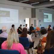 Participantes estão sentados em uma roda de conversa em uma sala moderna e iluminada. No painel projetado, lê-se “(Re)pensar Educação — Ética, tecnologia e humanização na escola”. Educadores e especialistas debatem o tema diante do público atento.