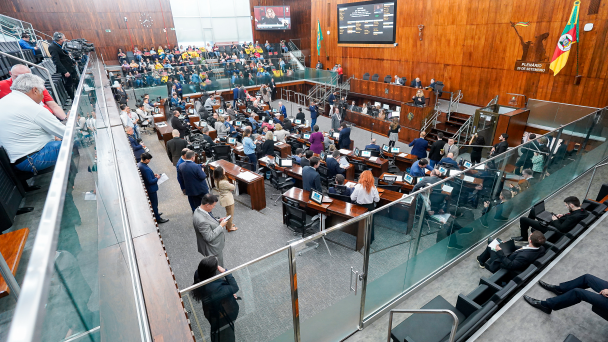 Imagem mostra uma votação na Assembleia Legislativa, com diversas pessoas sentadas ou em pé em suas mesas. Ao fundo, há um telão com a votação. 