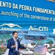 O governador Eduardo Leite aparece falando ao microfone, vestindo terno azul e camisa clara, diante de um grande painel azul com os logotipos da Aeromot e do AeroCITI. O painel traz o texto em português e inglês: “Lançamento da Pedra Fundamental do AeroCITI / Launching of the cornerstone of AeroCITI”.