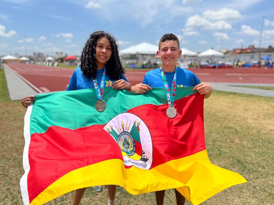 Foto mostra uma menina e um menino com suas medalhas e segurando a bandeira do Rio Grande do Sul