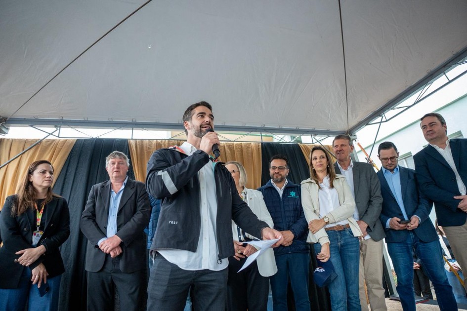 A imagem mostra o governador em pé, falando ao microfone. Ao fundo, também em pé, há diversas pessoas olhando para ele e acompanhando a fala.