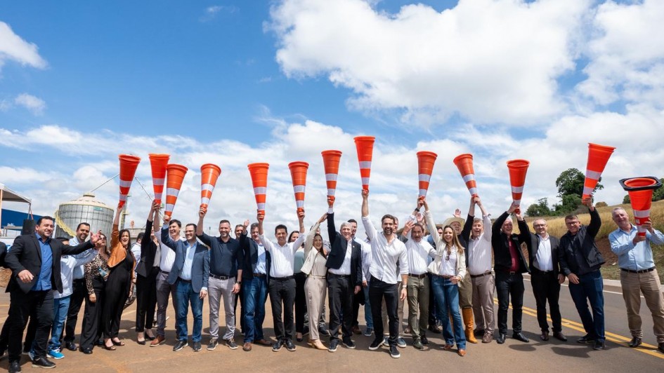 A imagem apresenta um grupo numeroso de pessoas alinhadas sobre o asfalto, segurando cones de sinalização laranja erguidos acima da cabeça.