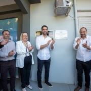 Governador Eduardo Leite inaugura reforma do pronto atendimento e entrega equipamentos a hospital em Mariano Moro com outras autoridades, em frente a uma placa. Eles sorriem e batem palmas.