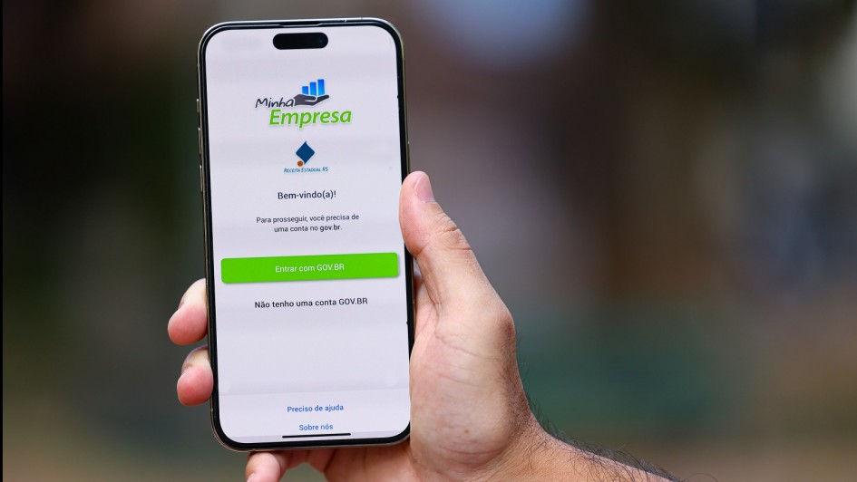 A imagem mostra uma mão segurando um smartphone. Na tela do celular aparece um aplicativo chamado Minha Empresa.