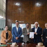 A foto mostra um grupo de cinco pessoas posicionadas atrás de uma mesa de madeira. No centro, duas pessoas seguram um papel. À esquerda, há um banner com o logotipo do BADESUL e a frase “A gente dá valor para o Rio Grande crescer”, acompanhada da marca do Governo do Estado do Rio Grande do Sul.