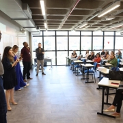 Foto exibe sala de aula com palestrantes, de pé à esquerda, e ouvintes participantes da formação sentados nas classes.