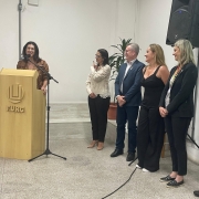 Foto mostra secretária discursando num púlpito com a logo da Furg. Ao lado dela, em pé, estão cinco pessoas, dois homens e três mulheres, que a observam atentamente.