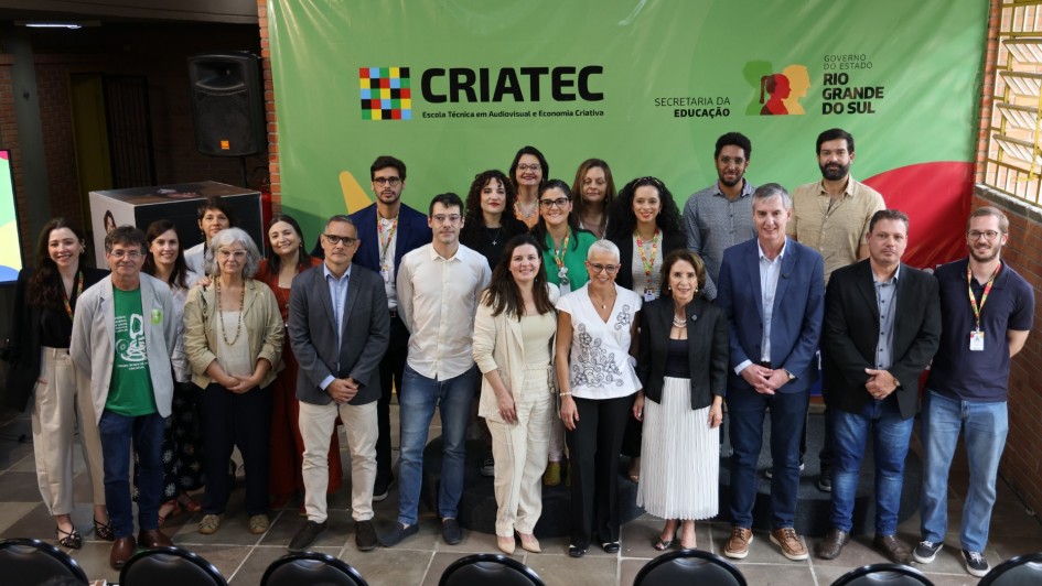 oto de grupo registra o lançamento do plano de ocupação da Escola Técnica CRIATEC, primeira voltada ao audiovisual e à economia criativa no Rio Grande do Sul. A imagem mostra autoridades, educadores e profissionais da cultura reunidos diante do painel institucional da CRIATEC, da Secretaria da Educação e do Governo do Estado do Rio Grande do Sul. Todos posam sorridentes em ambiente interno, com decoração colorida e iluminação natural.