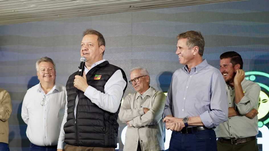 Foto de Edivilson falando ao microfone de pé, ao lado de mais três homens, que riem. Um deles é Polo.