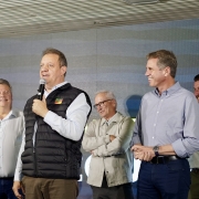 Foto de Edivilson falando ao microfone de pé, ao lado de mais três homens, que riem.