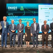 A foto mostra um grupo de oito pessoas alinhadas no palco, em frente a um painel digital com a identidade visual do evento ENAIQ 2025.