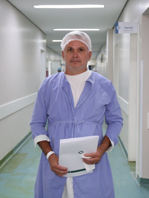 Homem de avental azul e touca hospitalar caminha por um corredor interno do hospital.