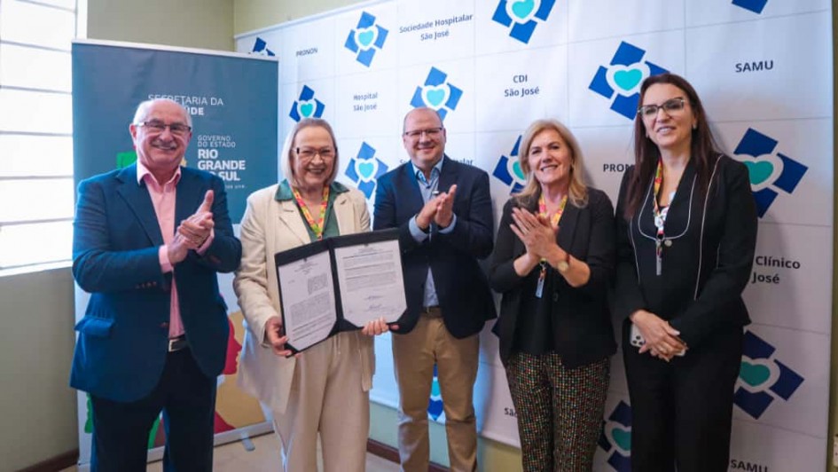 A imagem mostra cinco pessoas posando lado a lado. A secret&aacute;ria da Sa&uacute;de segura e exibe um documento assinado.
