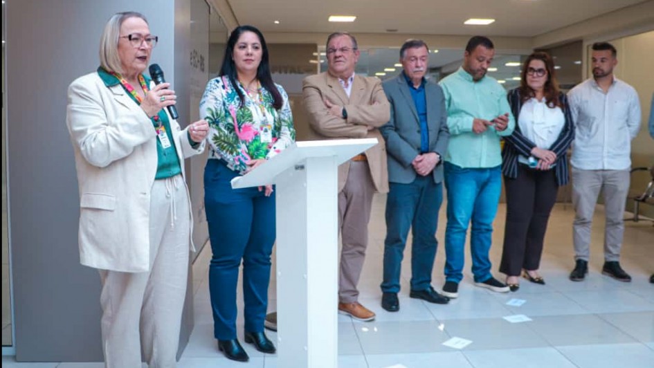 Foto de sete pessoas de pé em um evento. Elas estão enfileiradas. À esquerda, Arita fala segurando o microfone com a mão. Há um púlpito branco à frente.