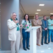 Foto de sete pessoas de pé em um evento. Elas estão enfileiradas. À esquerda, Arita fala segurando o microfone com a mão. Há um púlpito branco à frente.