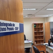 A imagem mostra a porta de uma sala com mesas de escritório, computador, cadeiras e estantes. Na porta, em destaque, se lê "Central Integrada de Alternativas Penais - CIAP". 