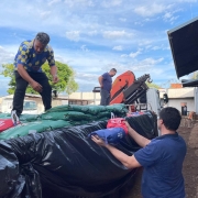 Pessoas descarregam sacos de produtos de caminhão com lona preta em área rural. Trabalho em equipe e esforço físico.