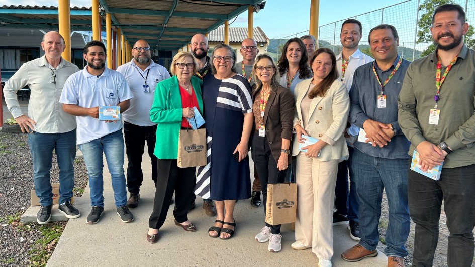 Foto posada de 14 pessoas ao ar livre, de pé, em ambiente escolar aberto, num pátio. A maioria sorri para a câmera.