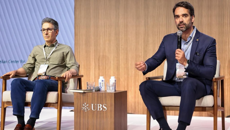 Foto mostra o governador Eduardo Leite (D), falando ao microfone, em evento, ao lado do governador de Minas Gerais