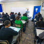 Foto mostra sala de aula com alunos acompanhando aula de professora.
