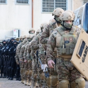 Uma foto em plano médio de seis pessoas (quatro mulheres e dois homens) posando juntas no momento da assinatura de um convênio ou portaria em Cruzeiro do Sul. Elas estão em frente à entrada de um prédio moderno e recém-reformado (possivelmente uma Unidade de Referência em Saúde - URS).

A mulher no centro, de blusa e blazer azul-claro sobre calça escura, segura o documento assinado. Ela é ladeada por cinco outras pessoas que estendem as mãos em direção ao documento, sorrindo. O homem ao lado esquerdo dela veste uma camisa polo bege, e o homem ao lado direito veste uma camisa social azul-clara. A mulher na extrema direita está vestida com um longo vestido rosa vibrante e um colar de miçangas coloridas.

O cenário é em frente a um edifício de dois andares com fachada branca e azul-clara. Uma escadaria de acesso com corrimões brancos está visível à direita. No canto esquerdo, há mastros com as bandeiras do Brasil, do Rio Grande do Sul e de Cruzeiro do Sul. O grupo está de pé sobre um tapete ou plataforma escura. O evento ocorreu ao ar livre, no final da tarde ou começo da noite, com boa iluminação frontal.