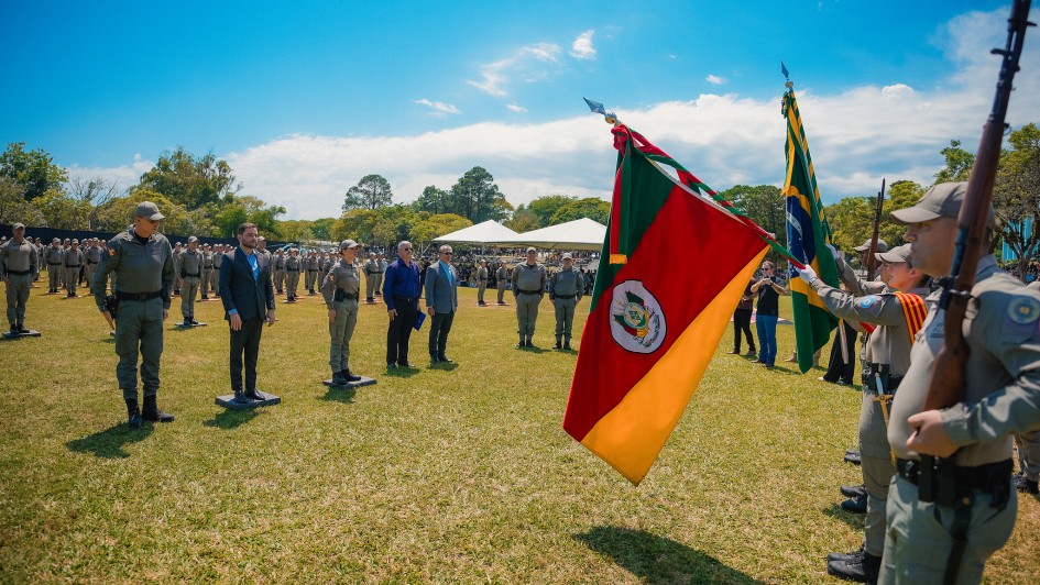 Foto mostra solenidade de formatura com policiais militares conduzindo as bandeiras do Estado e do Brasil