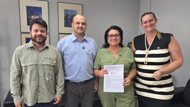 A imagem mostra quatro pessoas em pé, reunidas para a foto. A titular da Sema segura e exibe um documento assinado. 