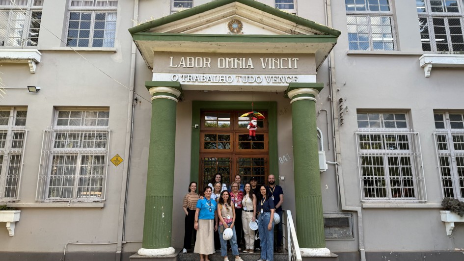 Foto mostra fachada do Colégio Onofre Pires, em Santo Ângelo com equipe da 14ª Coordenadoria Regional de Obras Públicas posando na entrada do prédio
