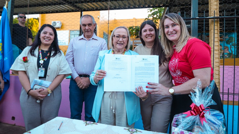 Foto mostra secretária Arita Bergmann, ao centro, segurando contrato, com duas pessoas na sua direita e outras duas pessoas à esquerda