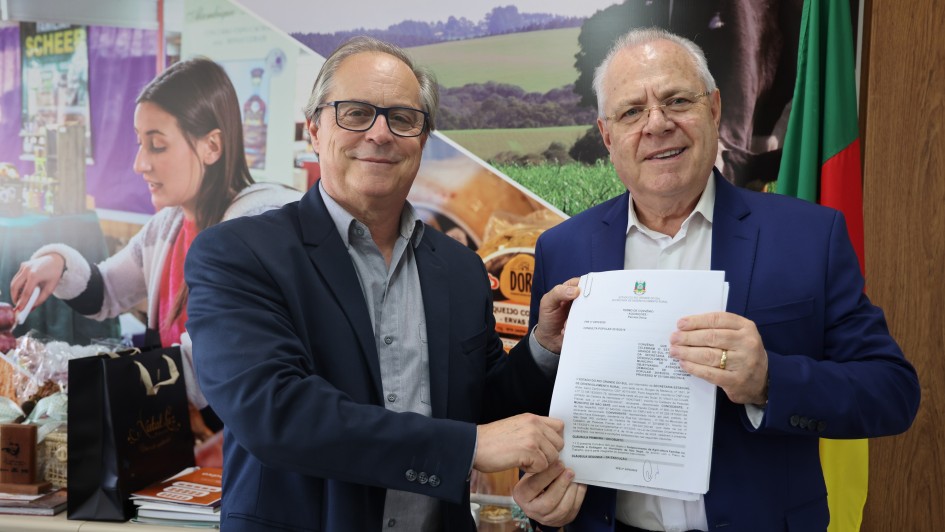 A imagem mostra dois homens segurando um documento assinado e posando para a foto. 